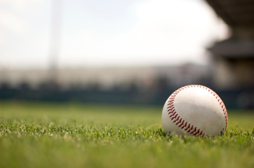 Baseball on grassy field with defocused stadium and sky in background