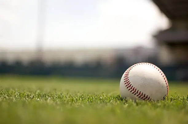 Baseball on grassy field with defocused stadium and sky in background