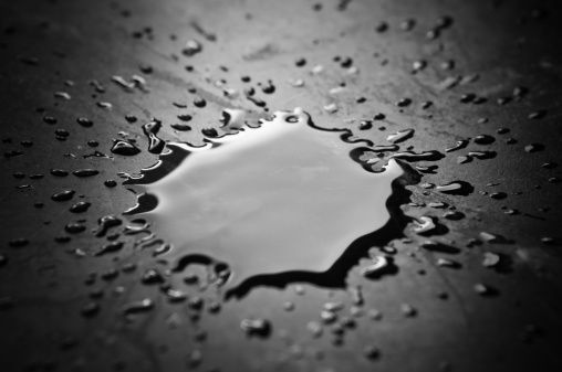 A puddle of liquid splattered on a black surface. It could be water, oil, or any other liquid.
