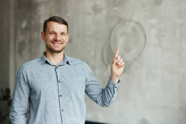 istock Happy male entrepreneur aiming at empty wall space in the office. 1477039334