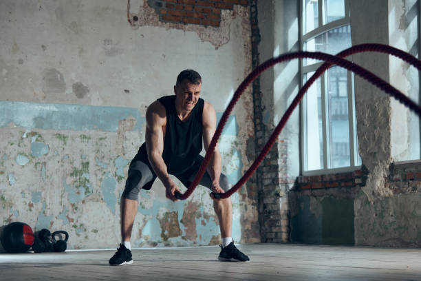 istock Strength, endurance and power. Muscular sportive young man doing functional exercises with battle ropes indoors. Concept of sportive lifestyle 1477039694