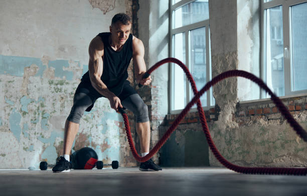 istock Strength and endurance. Young muscular man doing workout, training with battle ropes indoors. Functional training exercises. Concept of sportive lifestyle 1477039696