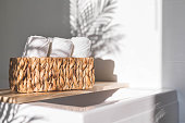 White bath towels rolled in woven jute basket on wooden shelf bathroom arrangement storage