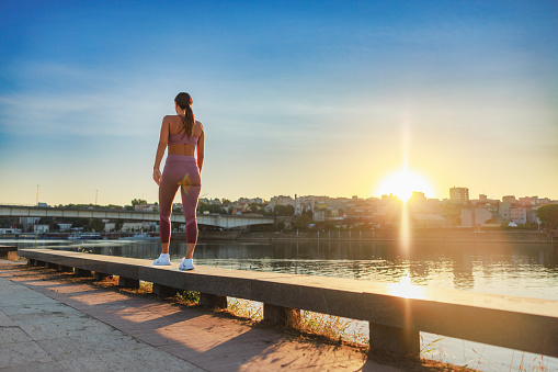 Woman in sports clothing walking on platform by the city river after jogging at dawn, outdoor fitness