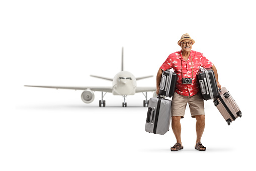Full length portrait of a mature man holding many suitcases in front of an airplane isolated on white background