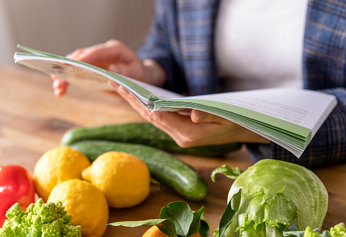 nutritionist studying a book with the theory of proper nutrition, vegetables on a table, lemons