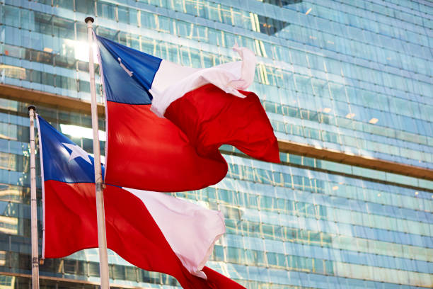 Two national flags blowing in the breeze with natural light reflecting on facade of modern office building in background.