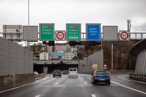 Lucerne, Switzerland; 26.03.2023: Road traffic in town, road signs on highway, cars driving to the entrance of tunnel. Swiss transportation infrastructure.