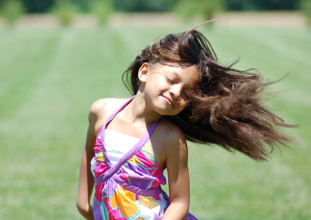 High angle view of a beautiful little girl smiling happily, reaching her hand towards the camera as if she is going to take it. Cute little girl sitting in a park on green grass.