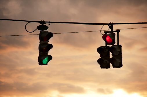 A red traffic light next to a green traffic light with textured morning clouds behind