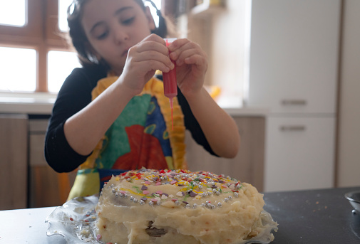 Little girl puts sprinkles on a birthday cake.