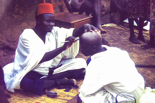 Yendi, Ghana - 1959: A man having his head shaved outdoors in Yendi, Ghana c.1959