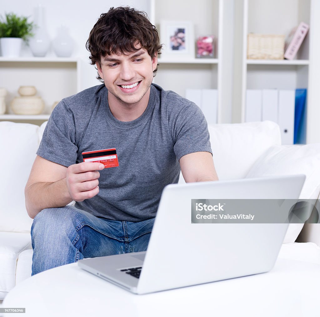 Man with credit card and laptop Handsome man holding credit card and using laptop for online shopping - indoors Adult Stock Photo