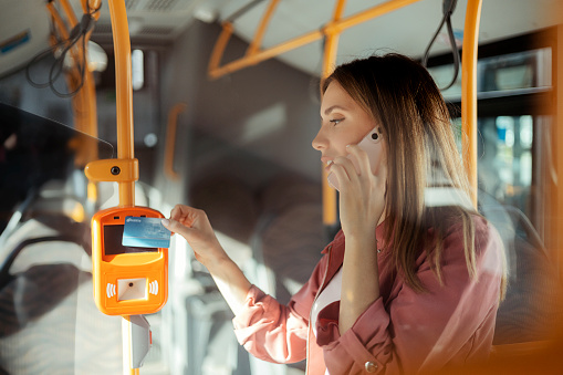 Young bearded man using ticket vending machine at outdoor public transport stop in autumn day