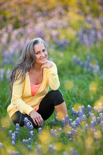 Attractive woman in her 50s kneeling in field of bluebonnets in Austin, Texas.