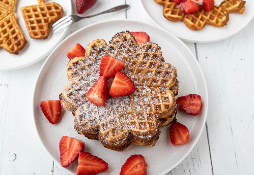 Delicious homemade heart shaped and stacked waffles with strawberry topping. Served on a plate on white table background from above.