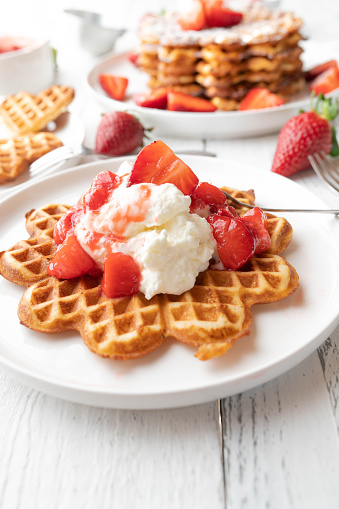 Delicious strawberry dessert for summer or mothers day with a fresh and homemade baked waffles. Topped with strawberry sauce and whipped cream. Served ready to eat on white table background.