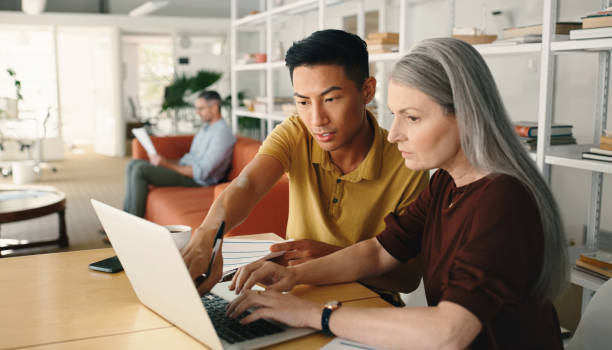 Laptop, training and business people in workspace for website design, IT support or planning startup project. Asian worker or person and manager, boss or woman on computer help with internet solution