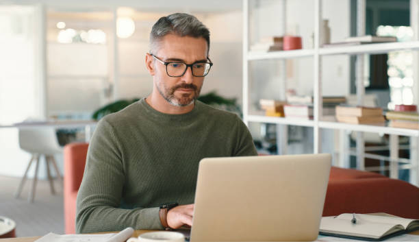istock Remote work, online and a mature man with a laptop for communication, entrepreneurship and business. Serious, internet and freelancer worker reading, planning and working on a computer at home 1477080026
