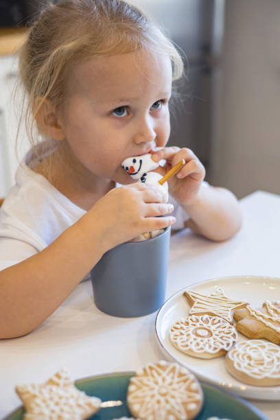 istock Little cute children eats a marmmello snowman decorated with icing and drinks cocoa. 1477081809