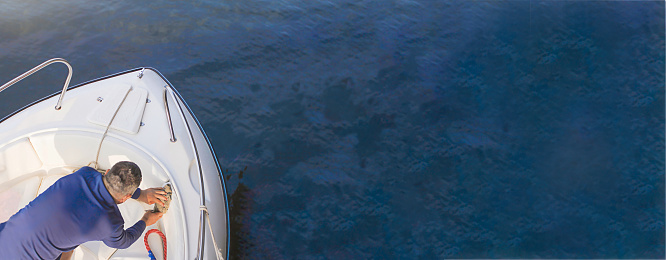 A male sailor washes a white boat. Yacht maintenance concept. Summer banner on the sea. top view