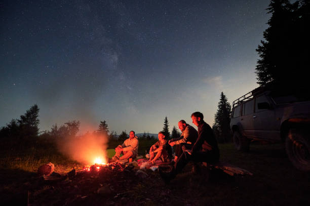 istock Group of hikers sitting near campfire under night sky. 1477082877