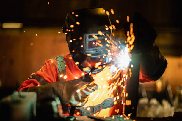 nahaufnahmen, die industrieuniformen tragen und ein lichtbogenschweißgerät verwenden, um stahl in der fabrik zu schweißen. metallbauherstellung und bauinstandhaltungsservice nach handwerklichem fertigkeitsarbeitskonzept. - electric arc stock-fotos und bilder