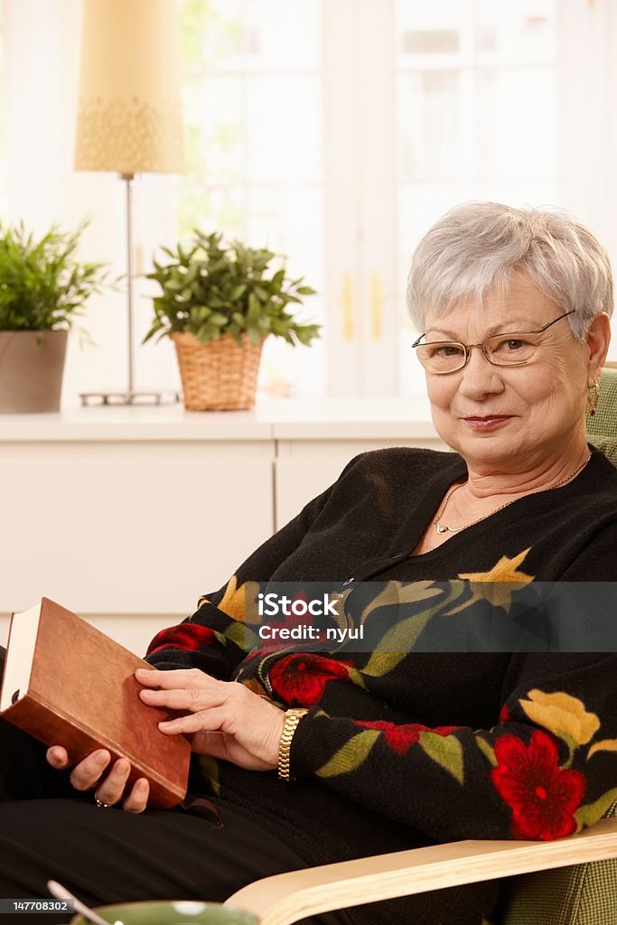 Idosos mulher na poltrona com livro - Foto de stock de 60 Anos royalty-free
