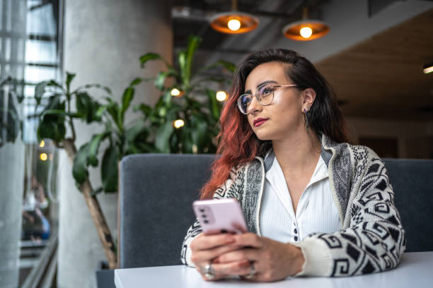 istock Young woman contemplating holding mobile mobile at office 1477086579