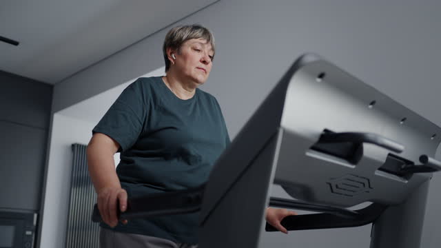 Senior Woman Listening To Music When Walking On Treadmill At Home, Cardio Workout For Be Healthy