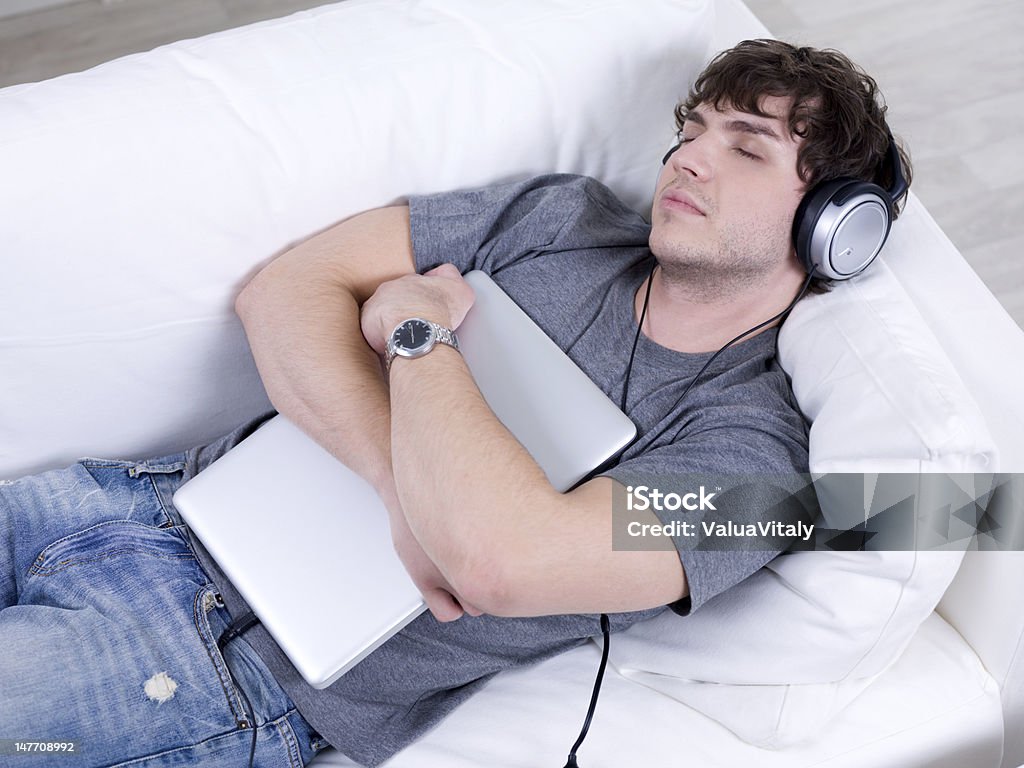 Sleeping man with headphone and laptop Man listening music in headphone and sleeping in embrace with laptop on the sofa 20-29 Years Stock Photo