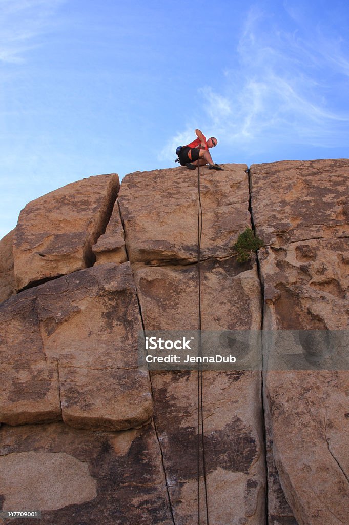 Killer day to rappel A young man gets ready to rappel down a cliff side against a killer sky. Adult Stock Photo