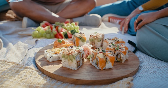 Sushi on wood plate, friends on picnic and fast food with social gathering, party and eating seafood together. Friendship, people relax and healthy lunch meal zoom with Japanese cuisine
