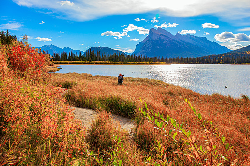 Elderly man with gray hair takes pictures of a beautiful landscape. Canada. Indian summer in the Rocky Mountains. Yellow autumn grass on the shores of mountain lake Vermillon.