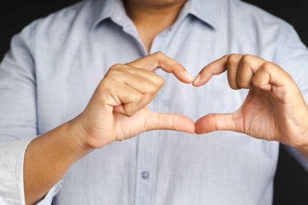 istock Man making heart figure love sign with fingers while standing on a black background. 1477100627
