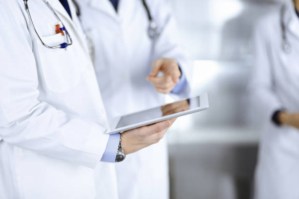 istock Group of unknown doctors use a computer tablet to check up some medical names records, while standing in a hospital office. Physicians ready to examine and help patients. Medical help, insurance in health care, best desease treatment and medicine concept 1477103108