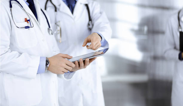 istock Group of unknown doctors use a computer tablet to check up some medical names records, while standing in a hospital office. Physicians ready to examine and help patients. Medical help, insurance in health care, best desease treatment and medicine concept 1477103111