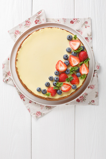 Classic Freshly New York Cheesecake with fresh berries and mint closeup on the plate on the wooden table. Vertical top view from above
