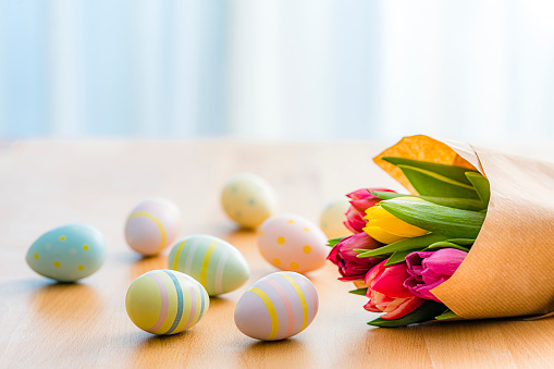 Close up view of painted Easter eggs and tulips shot on wooden table. The composition is at the bottom of an horizontal frame. Copy space. High resolution 42Mp studio digital capture taken with Sony A7rII and Sony FE 90mm f2.8 macro G OSS lens