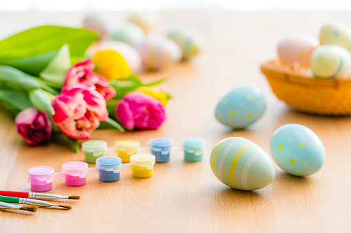 Close up view of painted Easter eggs, tulips, paint and paintbrushes shot on wooden table. Selective focus. High resolution 42Mp studio digital capture taken with Sony A7rII and Sony FE 90mm f2.8 macro G OSS lens