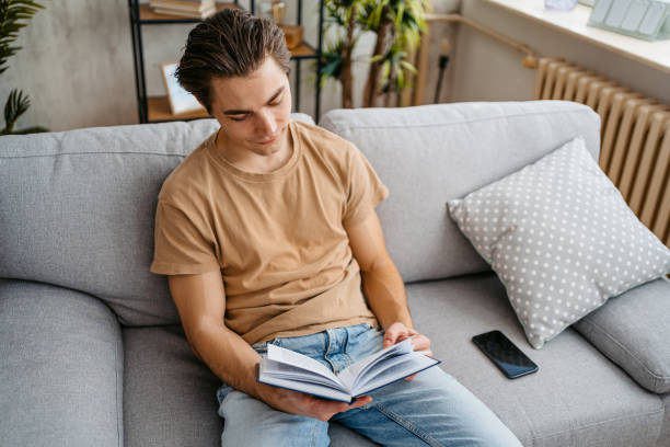 istock Young Man Reading A Book At Home 1477109393