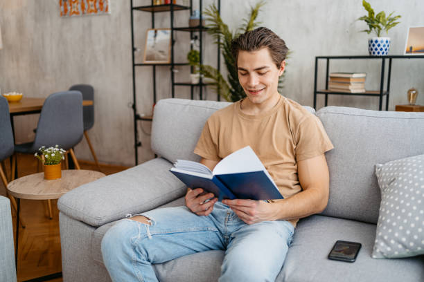 istock Young Man Reading A Book At Home 1477109884