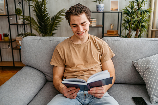 Handsome young man relaxing at home and reading a book.