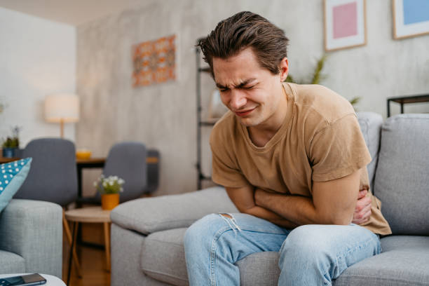 young man having stomach pain at home - indigestie fotos stockfoto's en -beelden