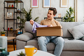 Young Man Unboxing A Package With A New Shirt He Ordered Online