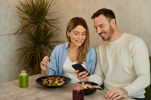 Mid adult couple enjoy eating salads and surfing the net on smart phone in salad bar