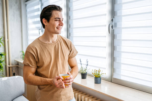 istock Young Man Drinking Coffee By The Window At Home 1477113991