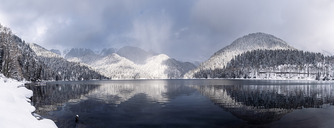 Beautiful winter landscape with mountain Ritsa lake and snow-covered trees along the shore. Great natural background with copy space for your design. Panoramic view.