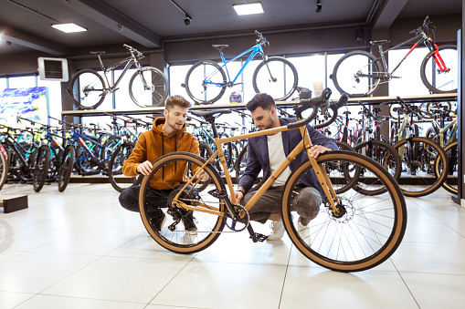 Salesman and young businessman watching bicycle in bike shop. Young man selling bikes.