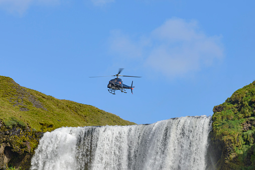 Skogafoss waterfall in Iceland on a summer's. A Helicopter fitted with a camera installation is flying over the waterfall.